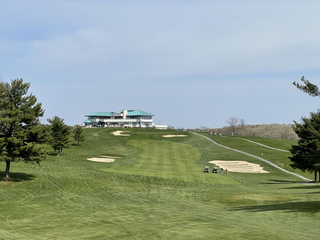 A clubhouse above a wide fairway with bunkers