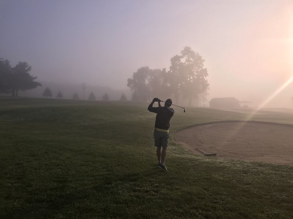 A golfer swinging through early morning fog