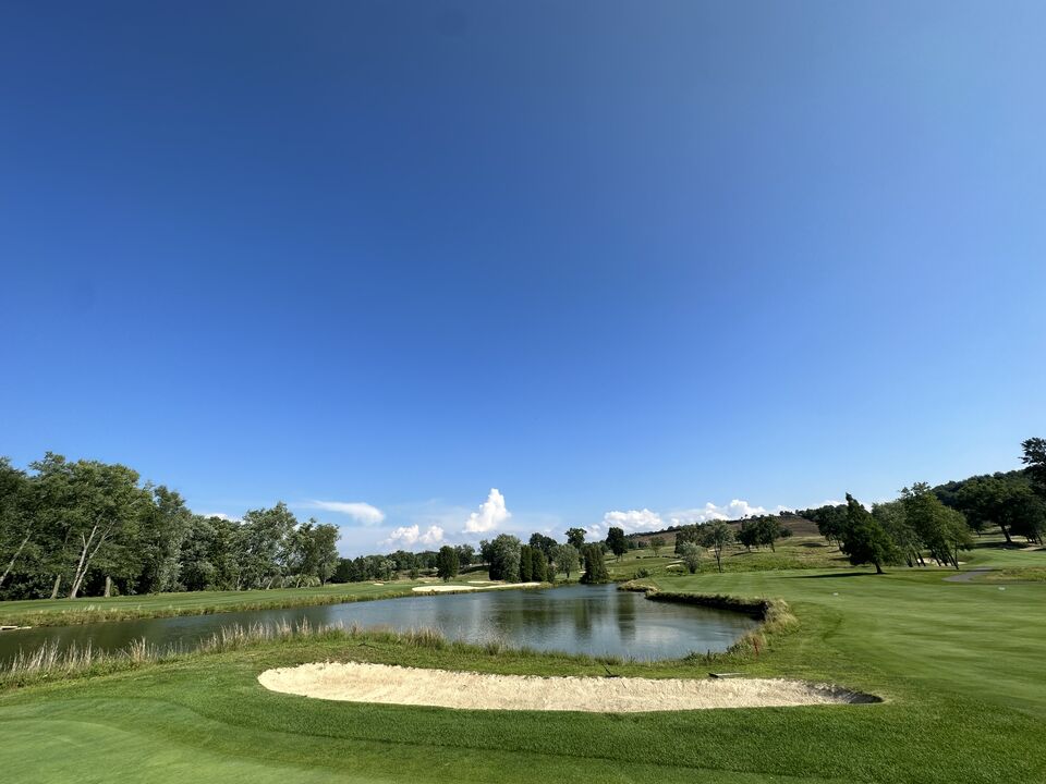 A pond guarding a green under a deep blue sky
